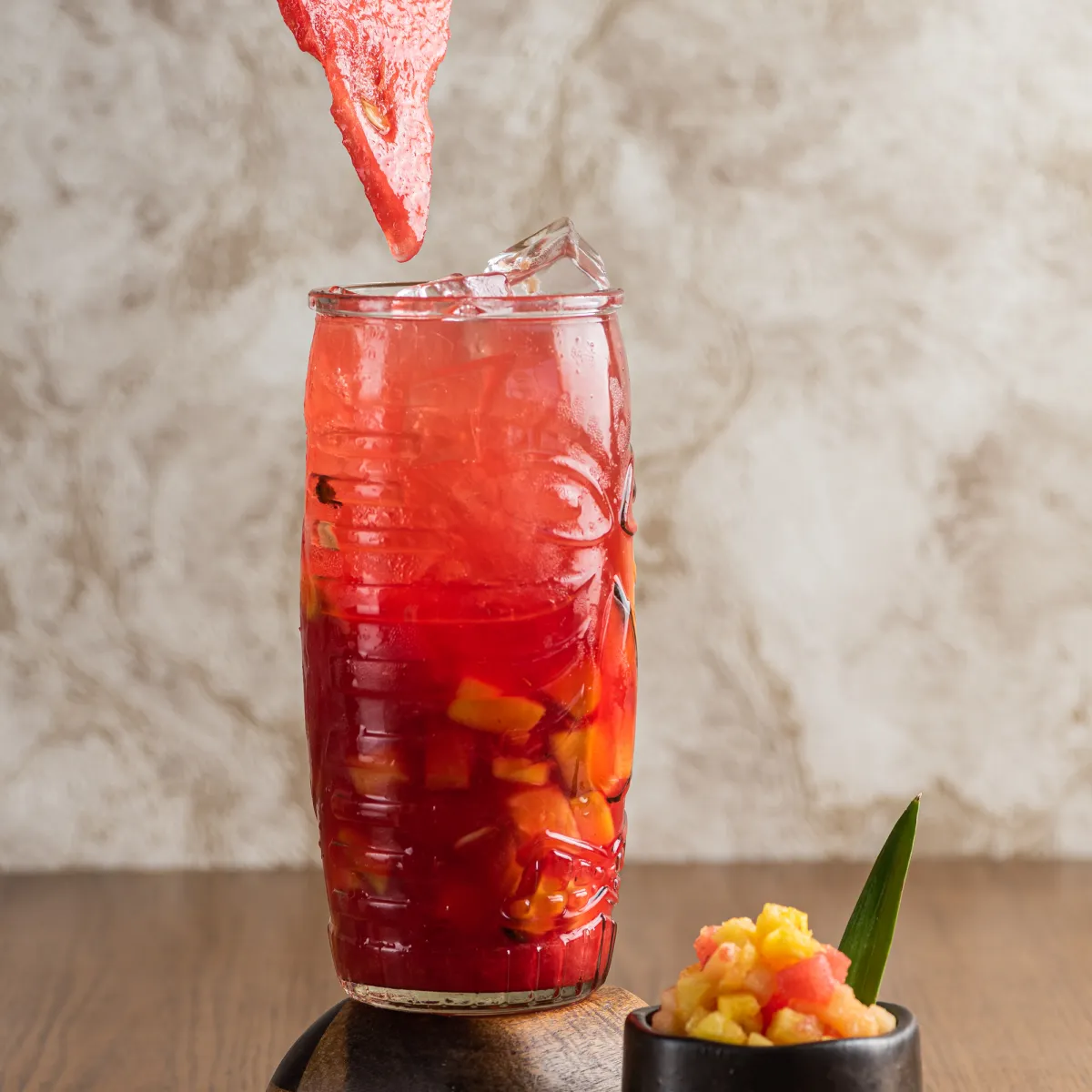 Bebida roja con fruta picada, hielo y rebanada de sandía decorativa arriba.