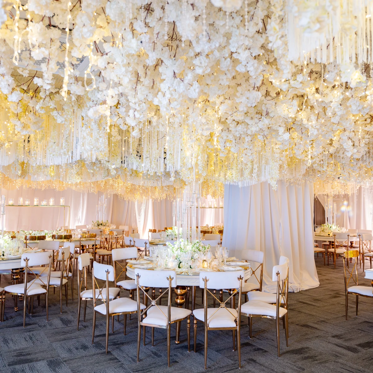 Sal&oacute;n decorado con flores blancas colgantes y mesas con sillas elegantes.