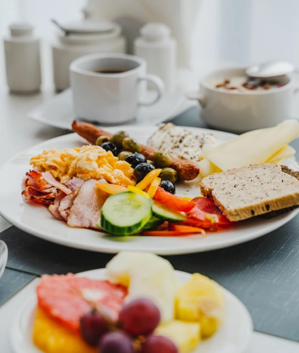 Desayuno variado con caf&eacute;, pan, frutas, embutidos y huevos revueltos.