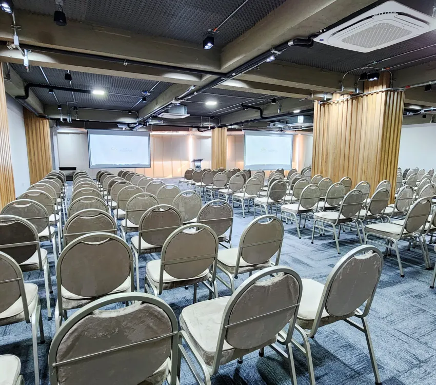 Sala de conferencias vac&iacute;a con sillas organizadas y pantallas al frente.