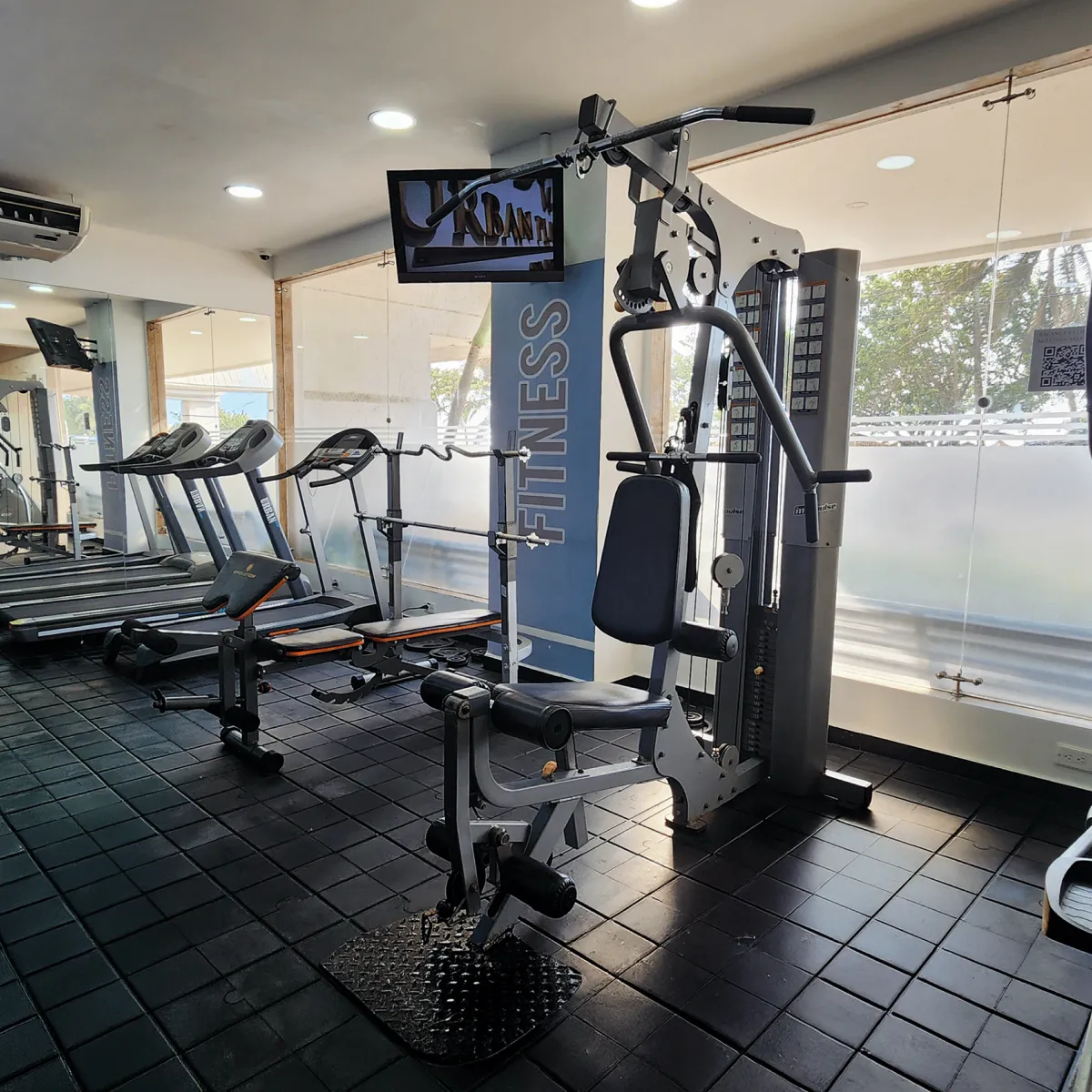 Gimnasio con equipo de ejercicio en una sala iluminada y espejos en la pared.