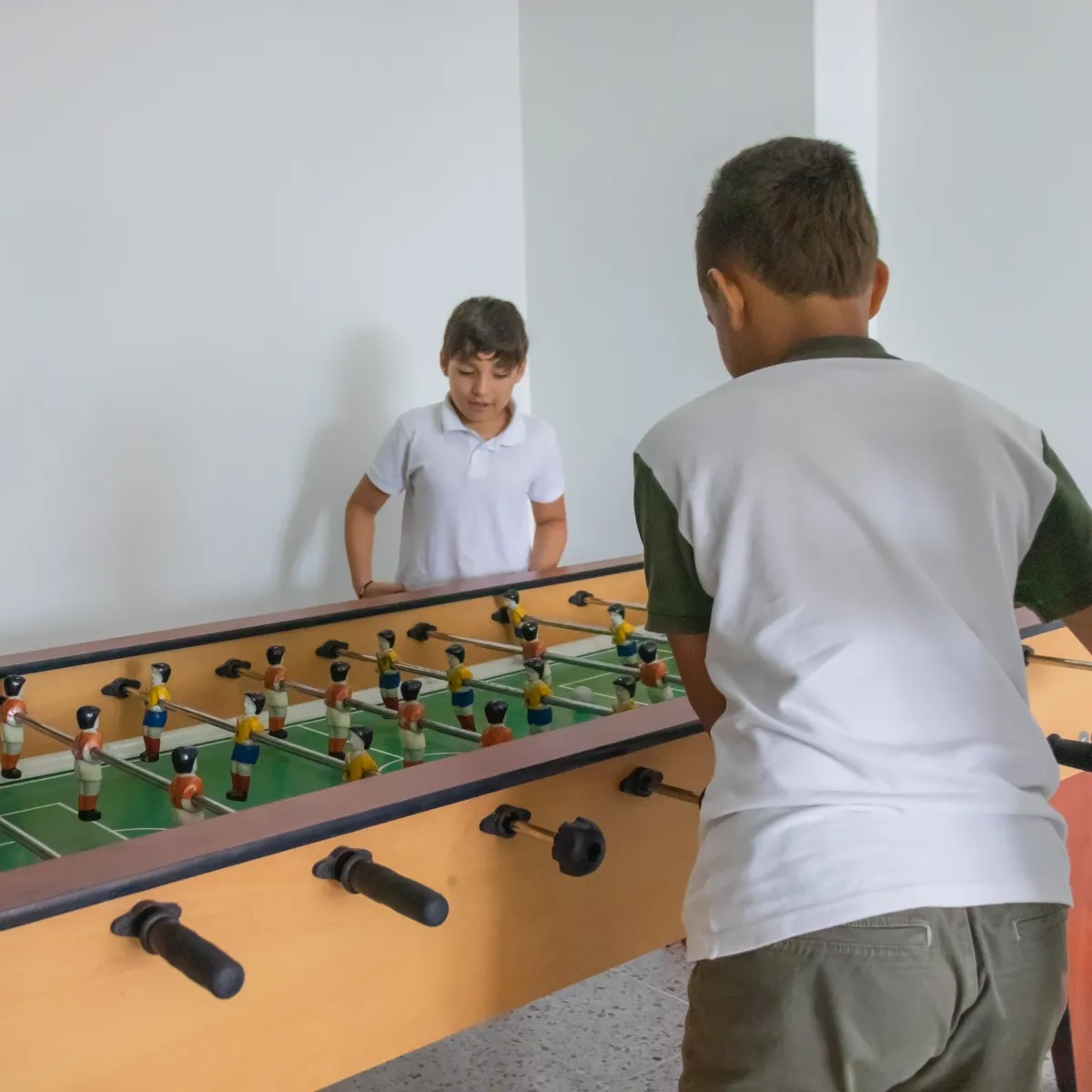 Niños jugando futbolín en una sala blanca.