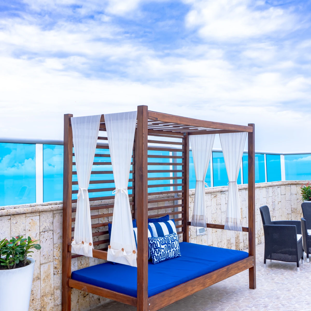 Cama con dosel y cojines, vista al mar y cielo parcialmente nublado.