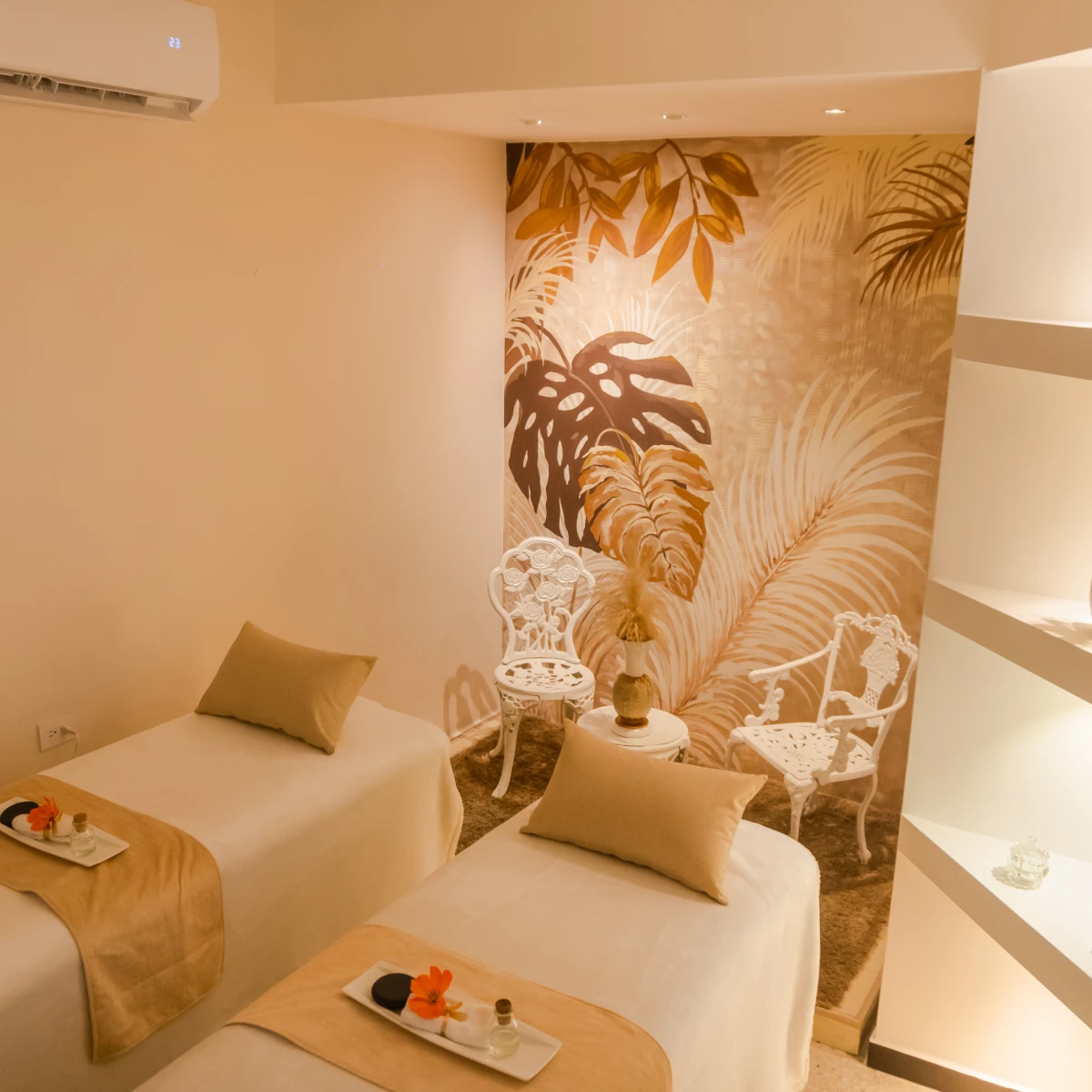 Sala de masaje con dos camas, decoración tropical y sillas blancas.