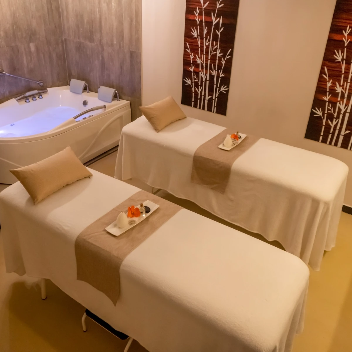 Sala de spa con dos camas de masaje y un jacuzzi al fondo.