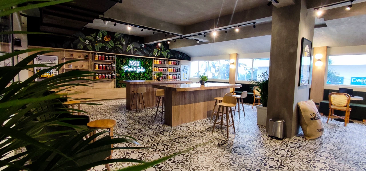 Cafeter&iacute;a moderna con mesas de madera y decoraci&oacute;n verde y tropical.