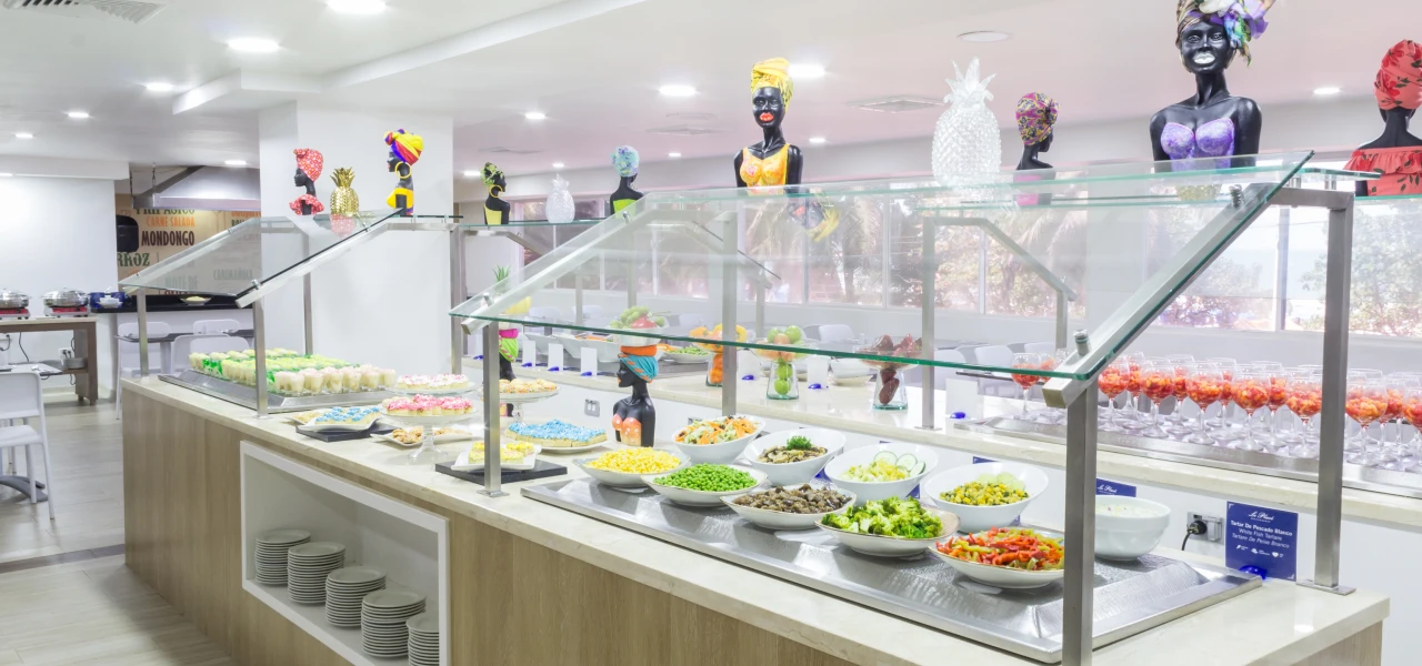 Buffet variado con ensaladas, postres y decoraciones coloridas en un comedor moderno.