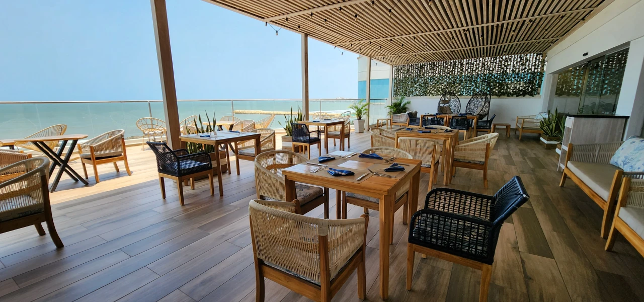 Terraza de restaurante con vista al mar y muebles de madera.