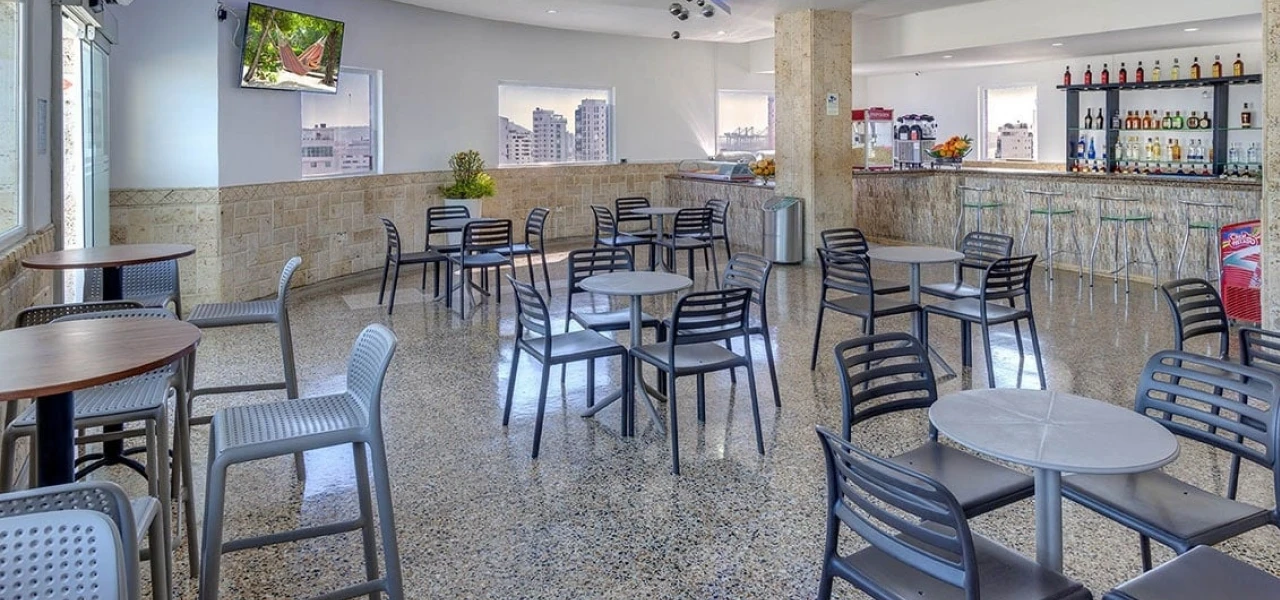 Cafeter&iacute;a moderna con sillas negras, mesas redondas y barra al fondo.