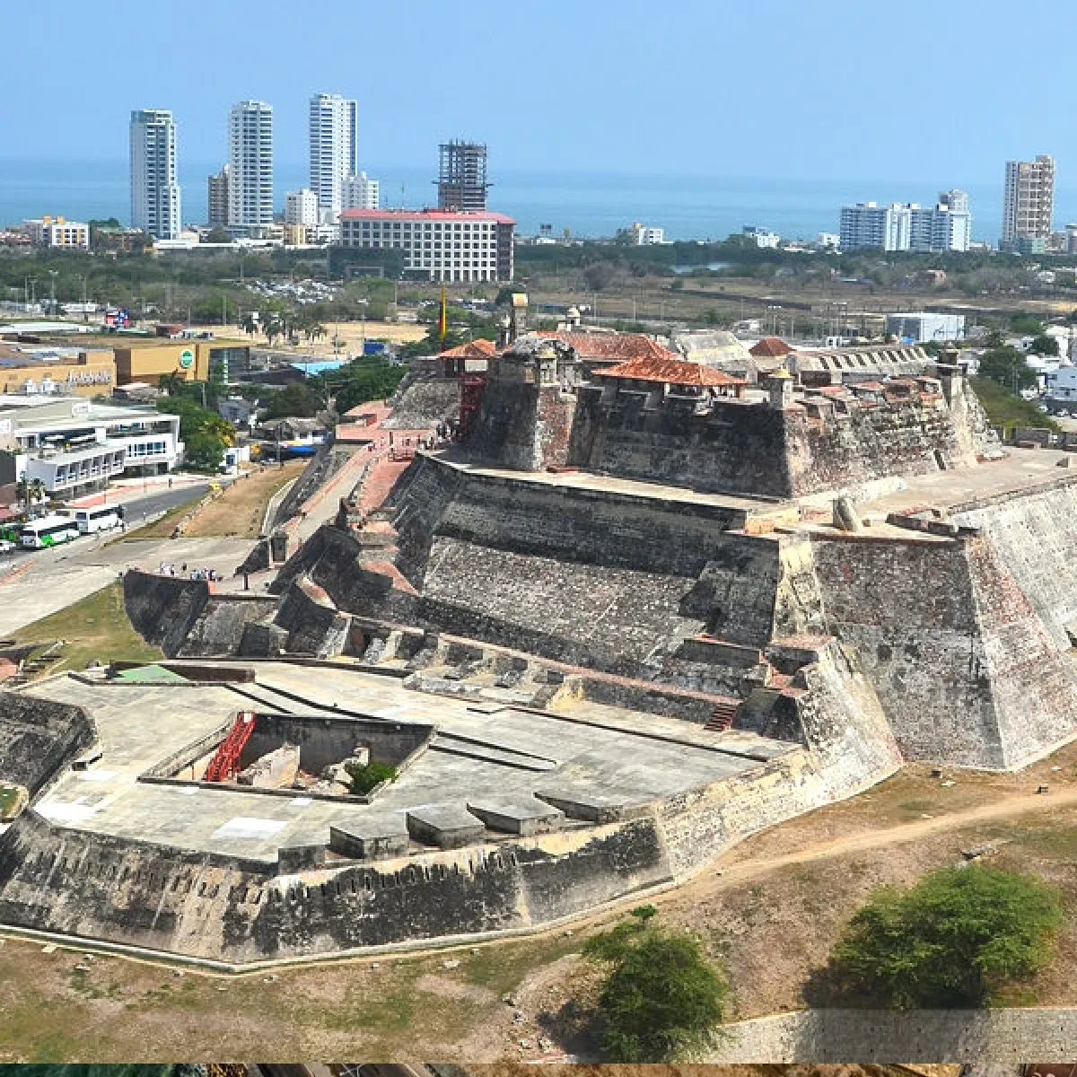 Fortaleza antigua frente a edificios modernos y mar.