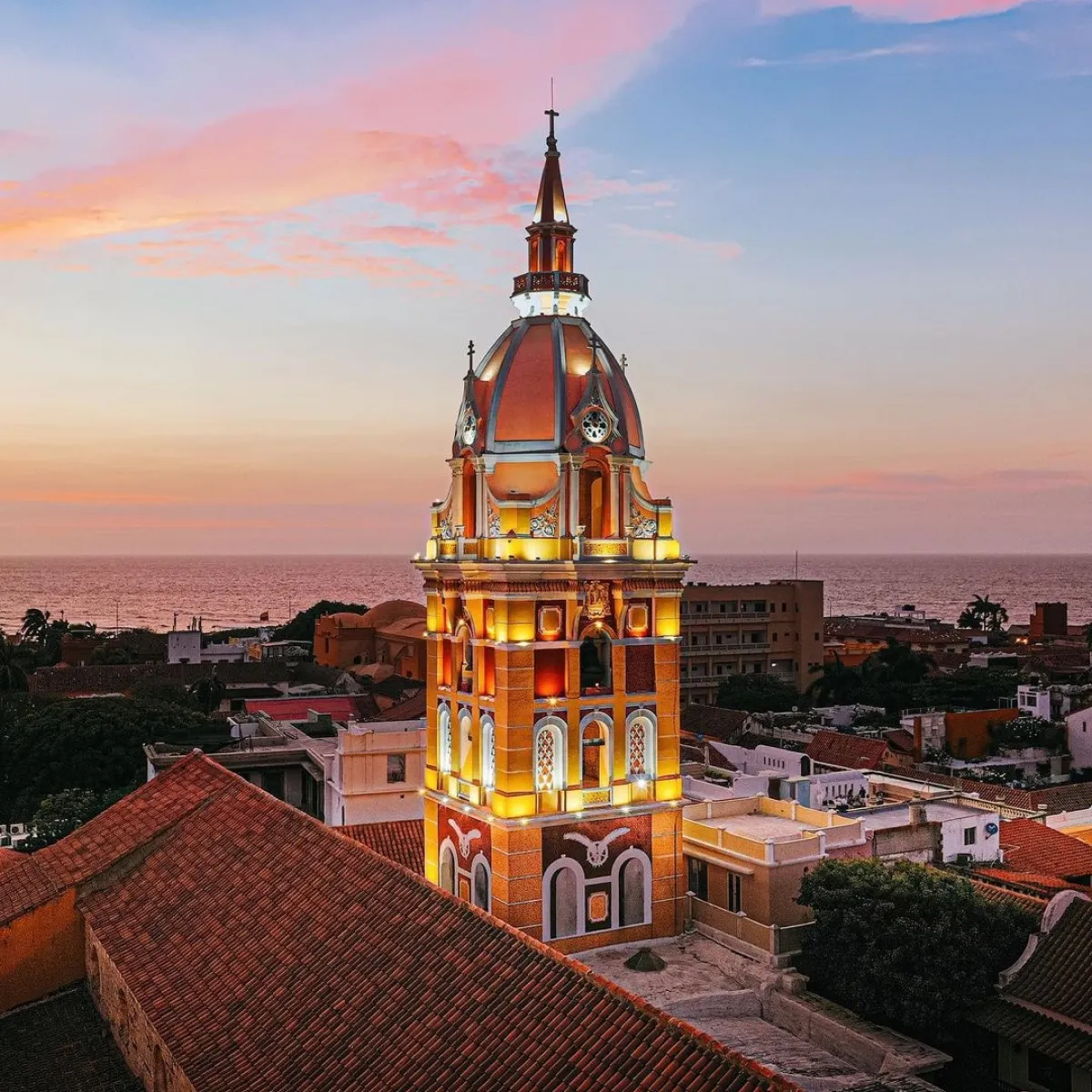 Torre iluminada al atardecer frente al mar y un cielo colorido.