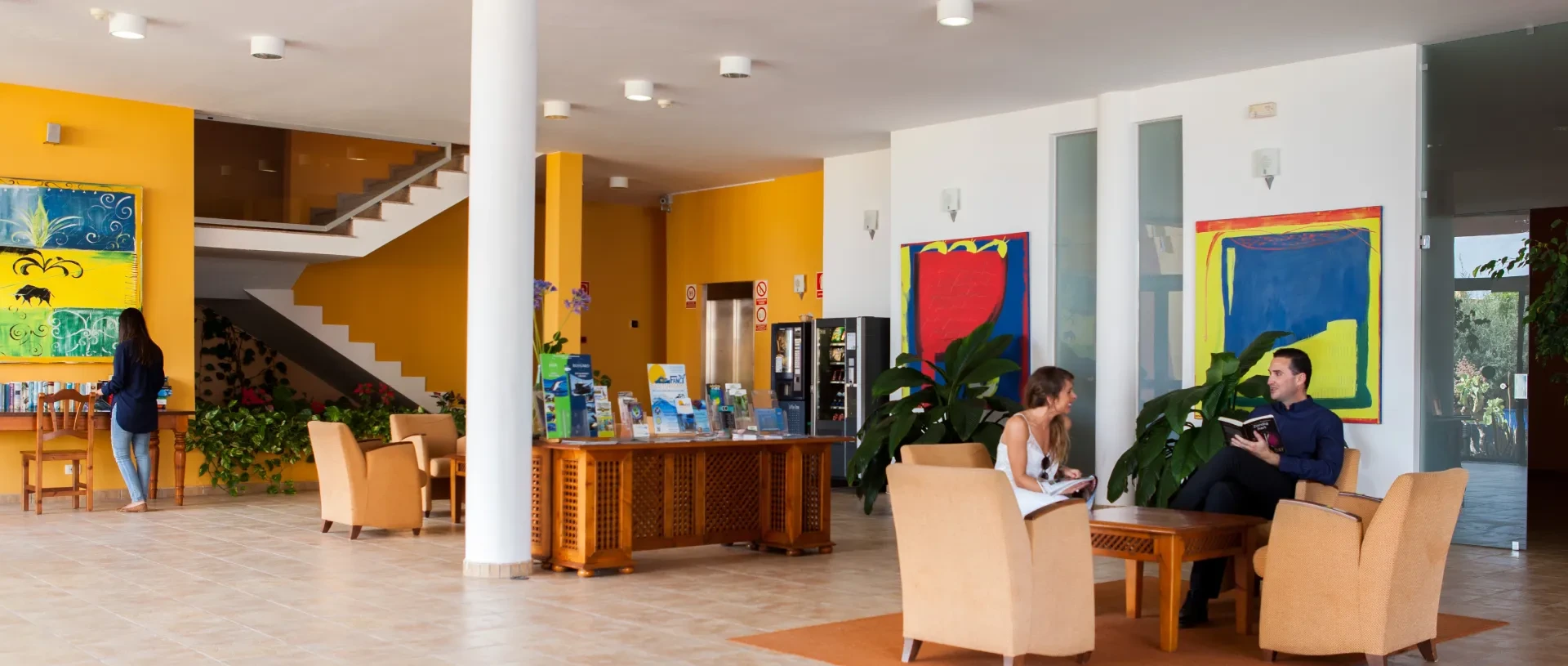 Vest&iacute;bulo colorido con muebles, cuadros y gente conversando.