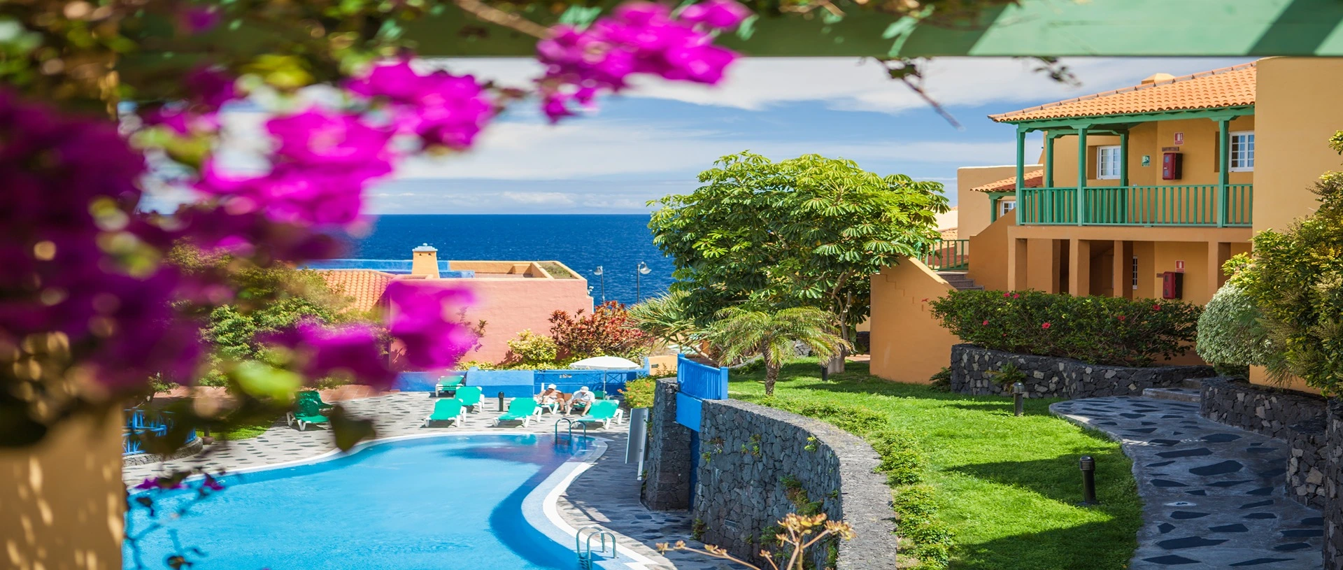 Piscina con casas coloridas y flores frente al mar.