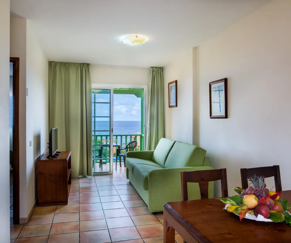 Sala luminosa con sof&aacute;, mesa de comedor y balc&oacute;n con vista al mar.