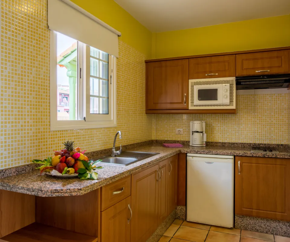 Cocina con muebles de madera, ventana, frutas, microondas y cafetera.