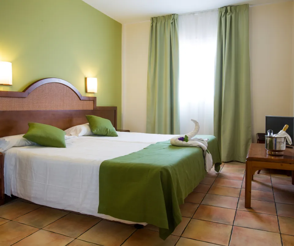 Habitaci&oacute;n de hotel con cama doble, decoraci&oacute;n verde y luz natural.