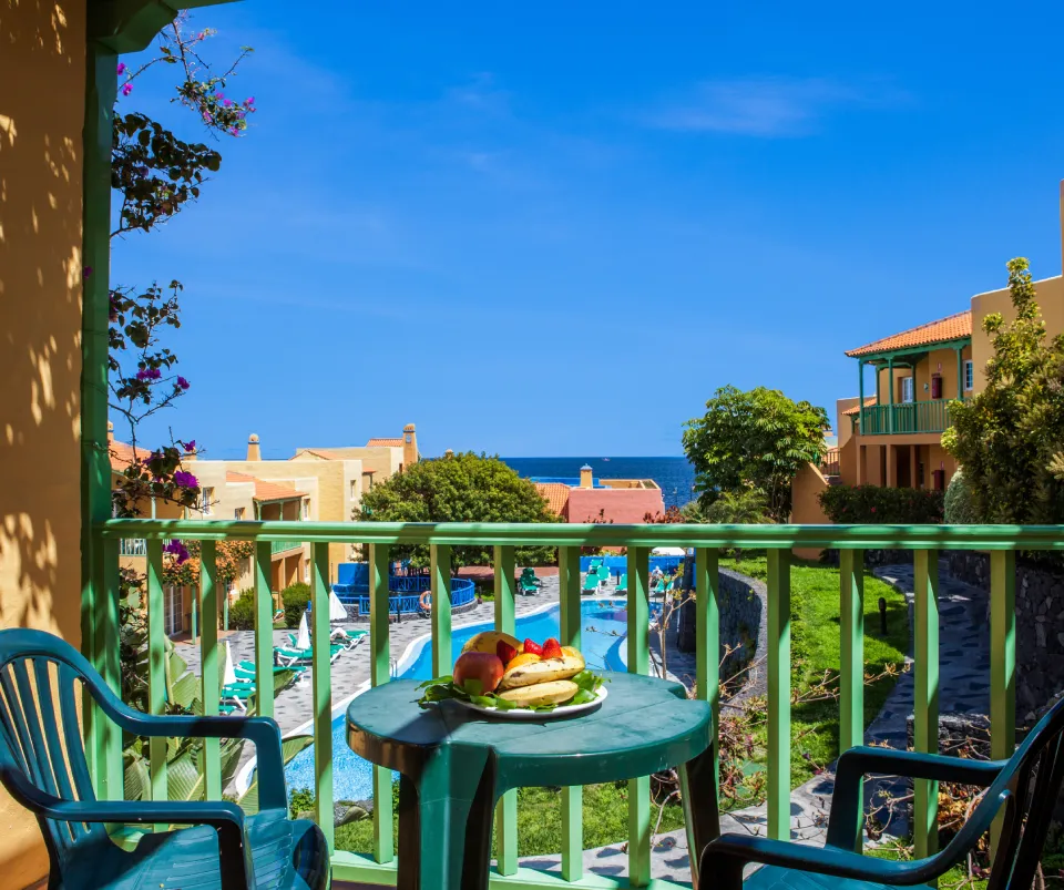 Vista desde un balc&oacute;n con piscina, edificios y mar de fondo.