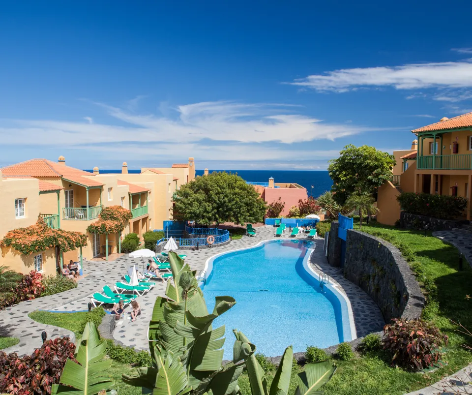 Complejo con piscina, tumbonas y vista al mar bajo un cielo azul claro.