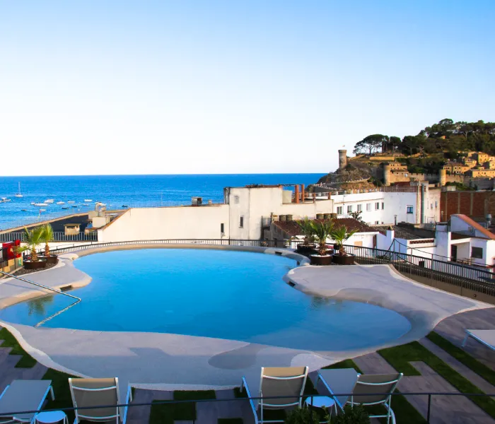 Piscina en una terraza con vista al mar y edificios, paisaje costero al fondo.