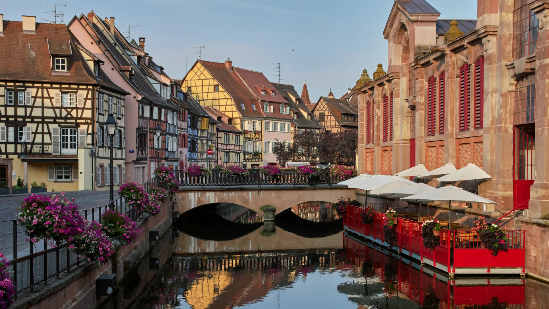 Maisons &agrave; colombages color&eacute;es et terrasse en bord de canal fleuri.