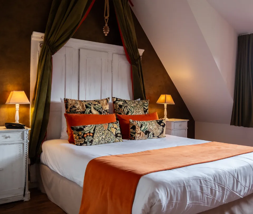 Chambre avec lit double, d&eacute;cor orange, lampes de chevet et coussins &agrave; motifs.
