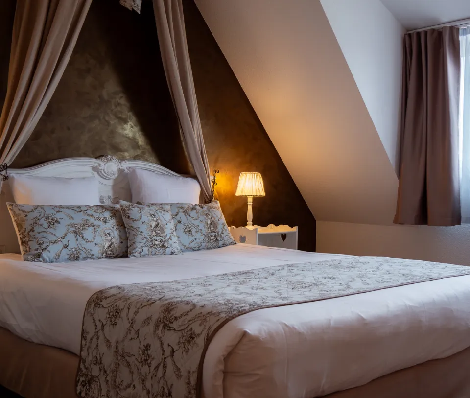 Lit &eacute;l&eacute;gant avec rideaux, lampe douce et oreillers fleuris dans une pi&egrave;ce cosy.