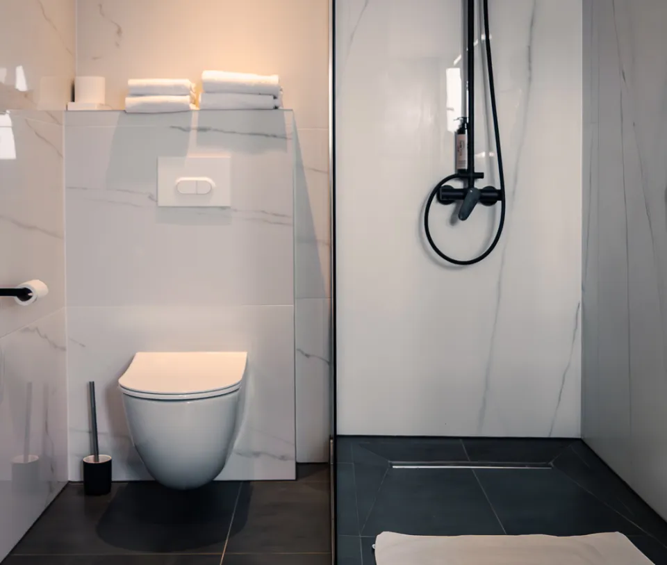 Salle de bain moderne avec toilettes et douche en carrelage blanc.