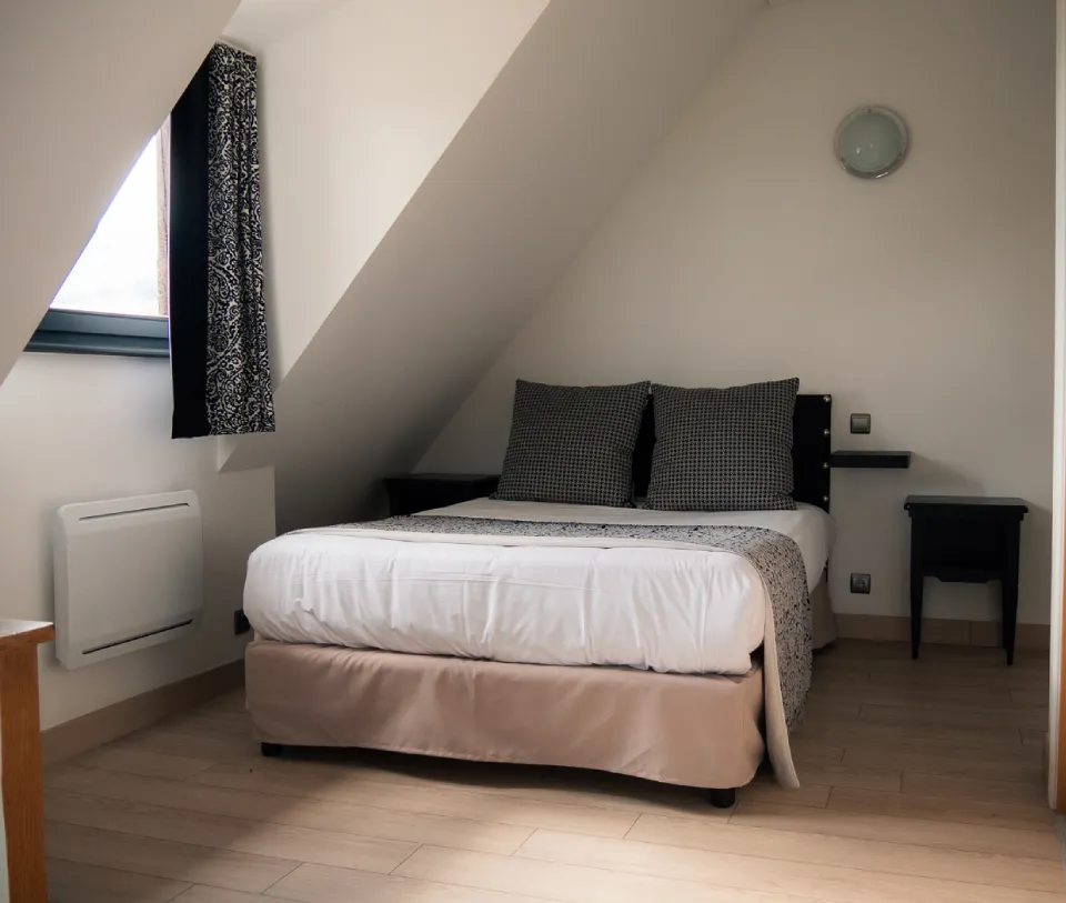 Chambre mansard&eacute;e avec lit double, tables de nuit et fen&ecirc;tre.