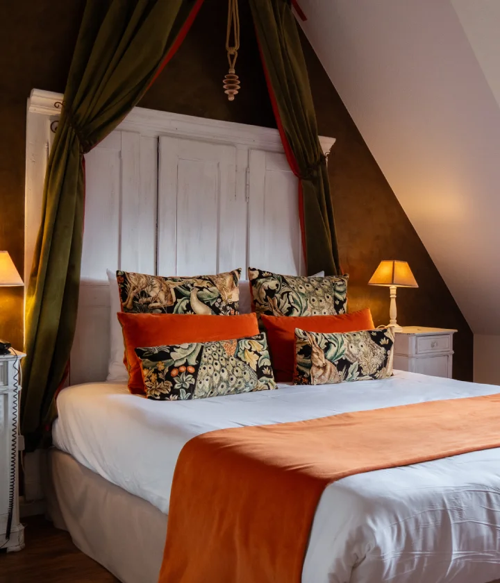 Chambre cosy avec lit &agrave; couvre-lit orange et coussins d&eacute;coratifs.