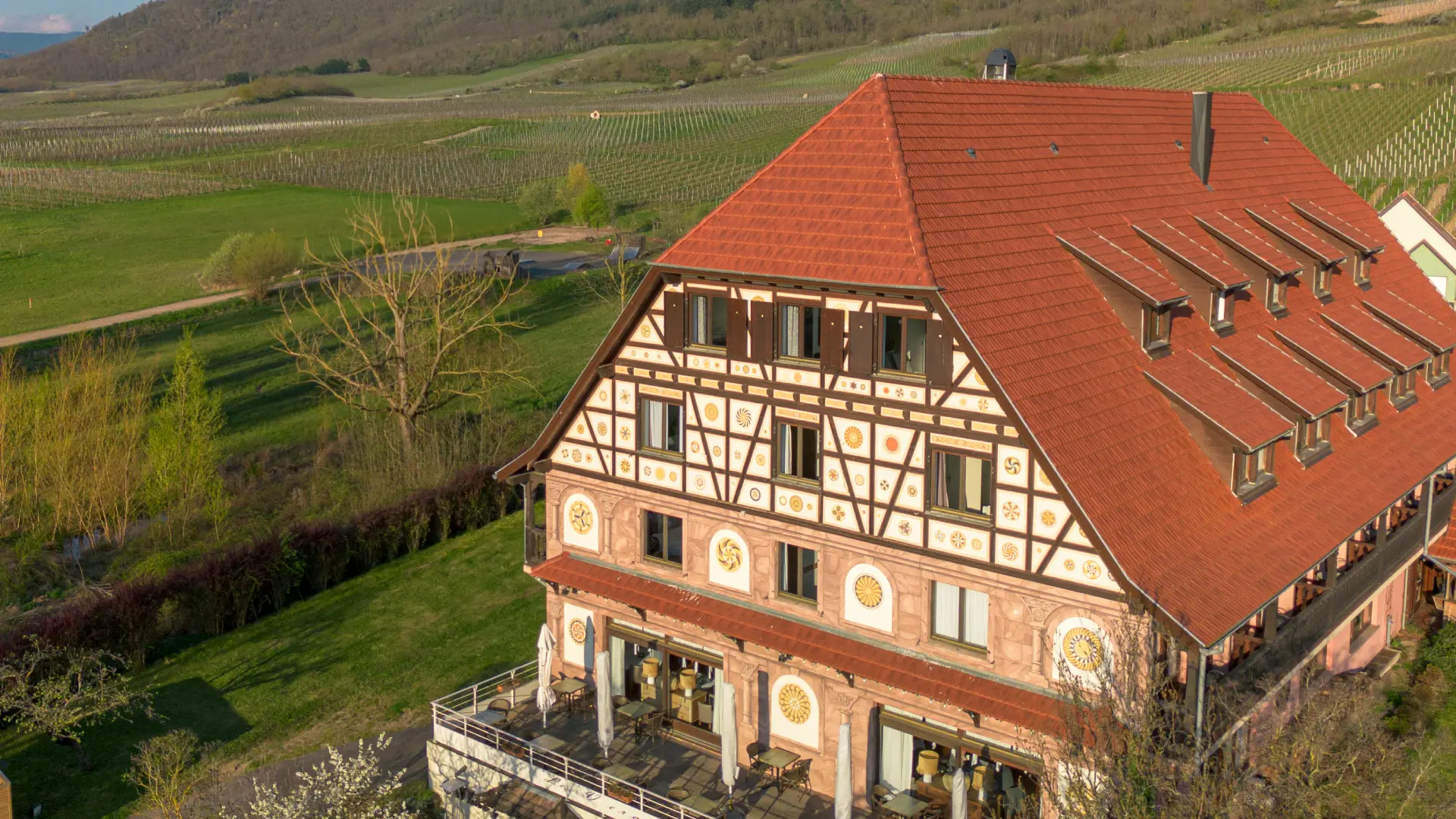Grande maison &agrave; colombages avec un toit rouge pr&egrave;s de champs et collines verdoyantes.