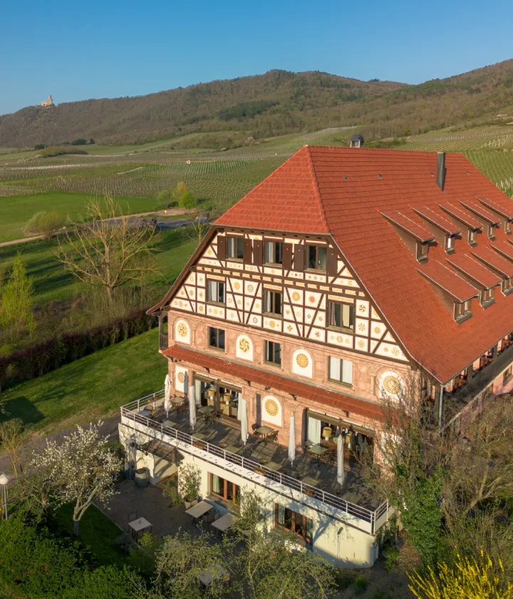 Grand b&acirc;timent &agrave; colombages entour&eacute; de vignobles et collines verdoyantes.