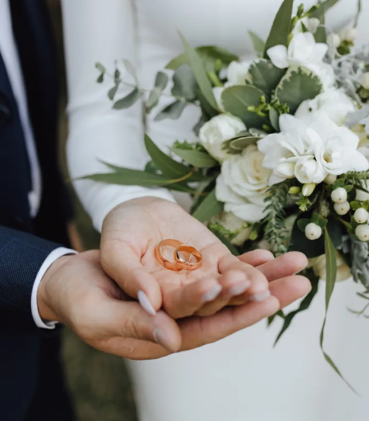 Deux alliances dans des mains, avec un bouquet de fleurs en arri&egrave;re-plan.
