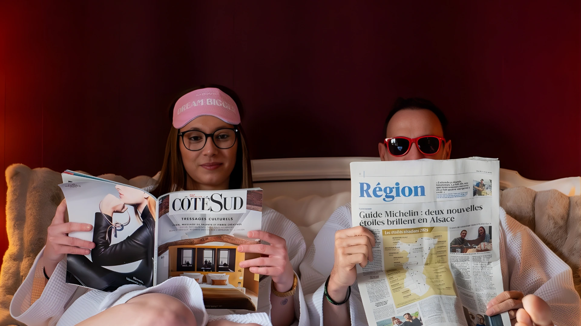 Deux personnes en peignoir lisent une revue et un journal au lit.