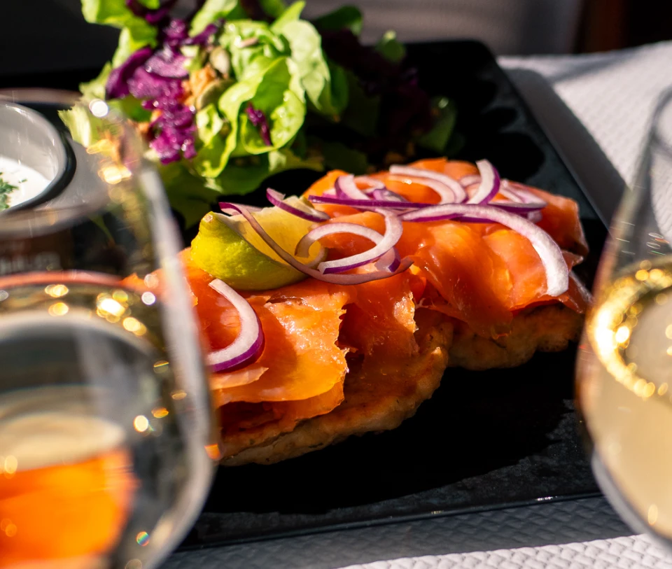 Assiette de saumon avec oignons rouges et salade, verres de vin &agrave; proximit&eacute;.
