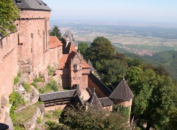 Ch&acirc;teau sur une colline bois&eacute;e avec vue sur la vall&eacute;e et le village.