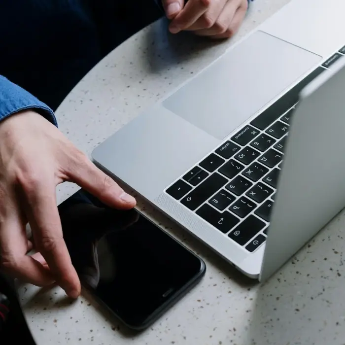 Manos usando un laptop y un smartphone sobre una mesa de oficina