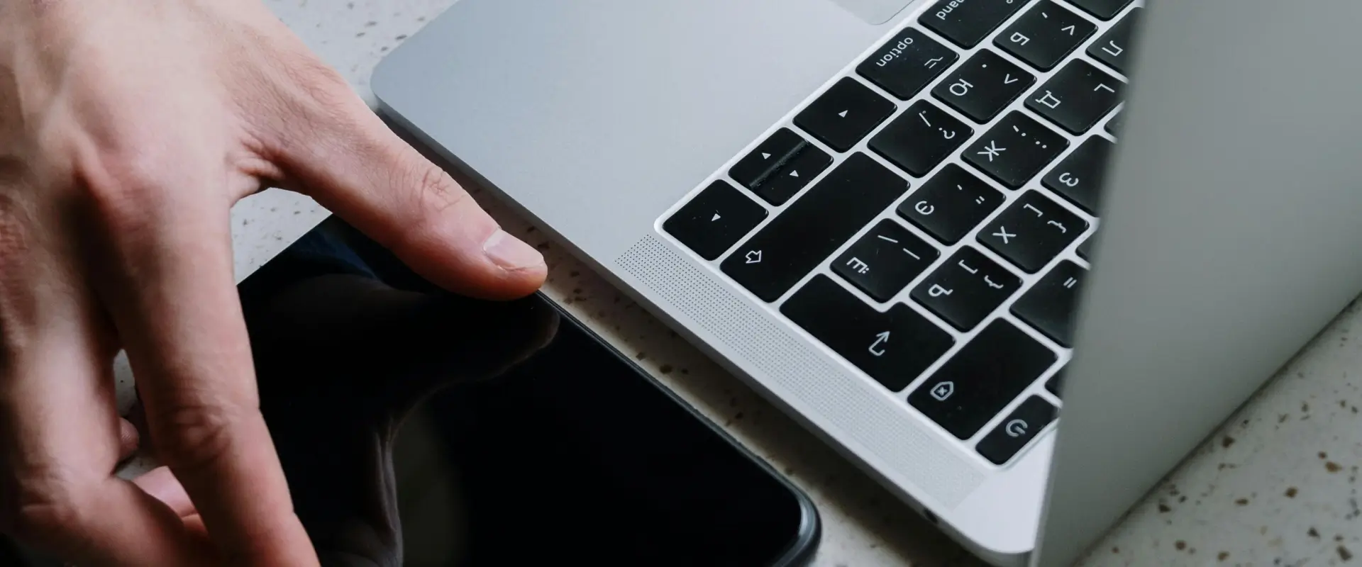 Mano presionando el teclado de un port&aacute;til en una mesa gris