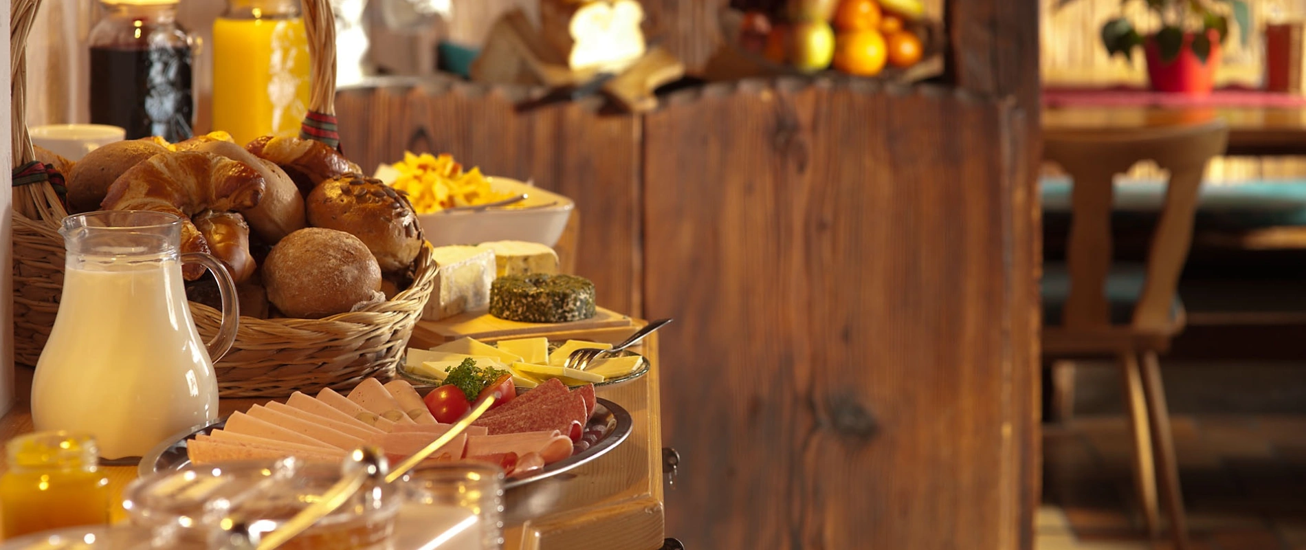 Desayuno en buffet: pan, queso y embutidos junto a jarra de jugo en madera