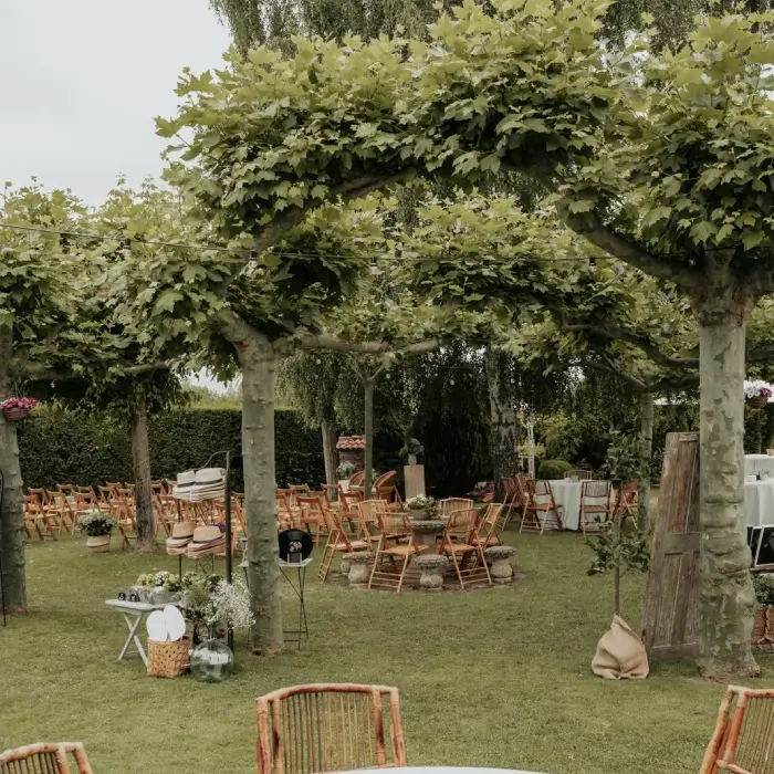 Jard&iacute;n con sillas y mesas bajo p&eacute;rgola de enredaderas y c&eacute;sped verde