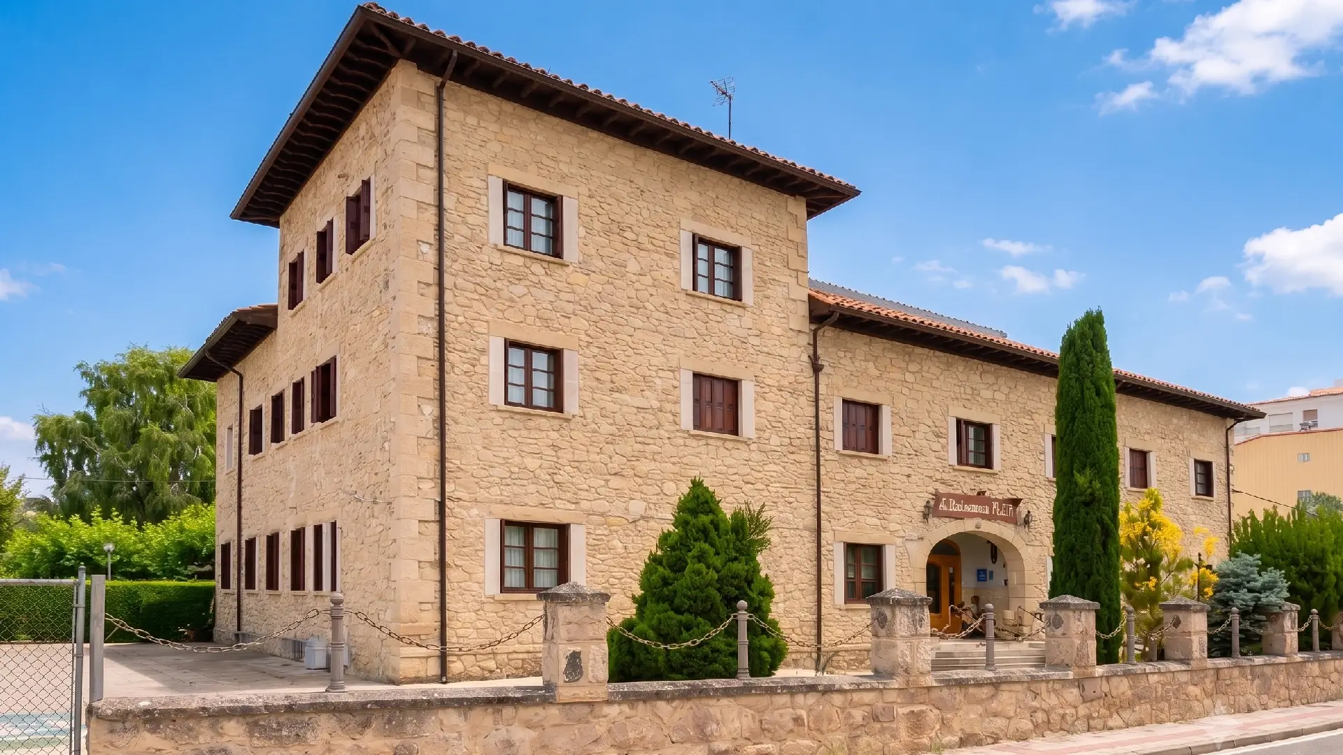 Fachada de casa de piedra con ventanas y jard&iacute;n bajo cielo azul