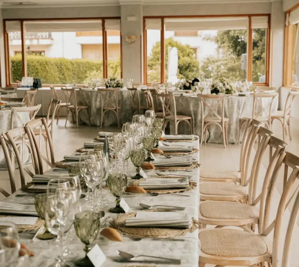 Mesa de banquete con cristaler&iacute;a y sillas en un sal&oacute;n con ventanas abiertas
