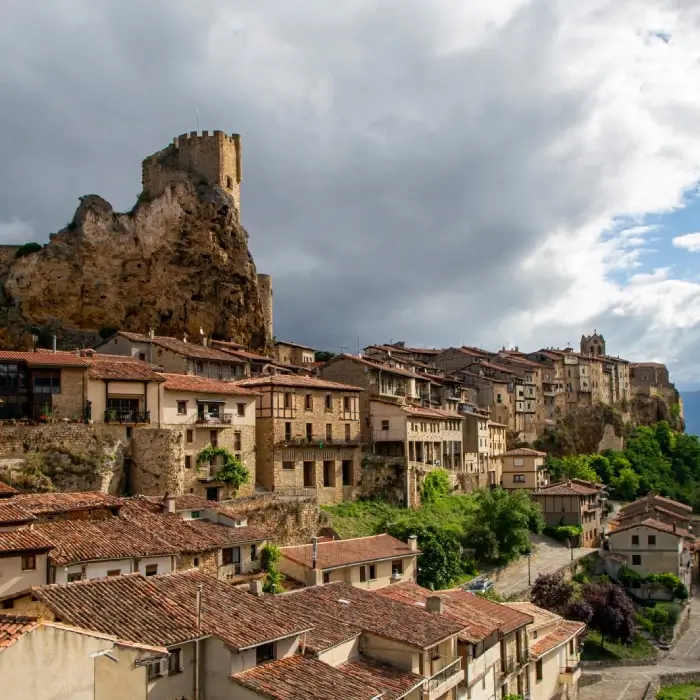 Pueblo medieval con torre y casas de tejados rojos bajo cielo nublado