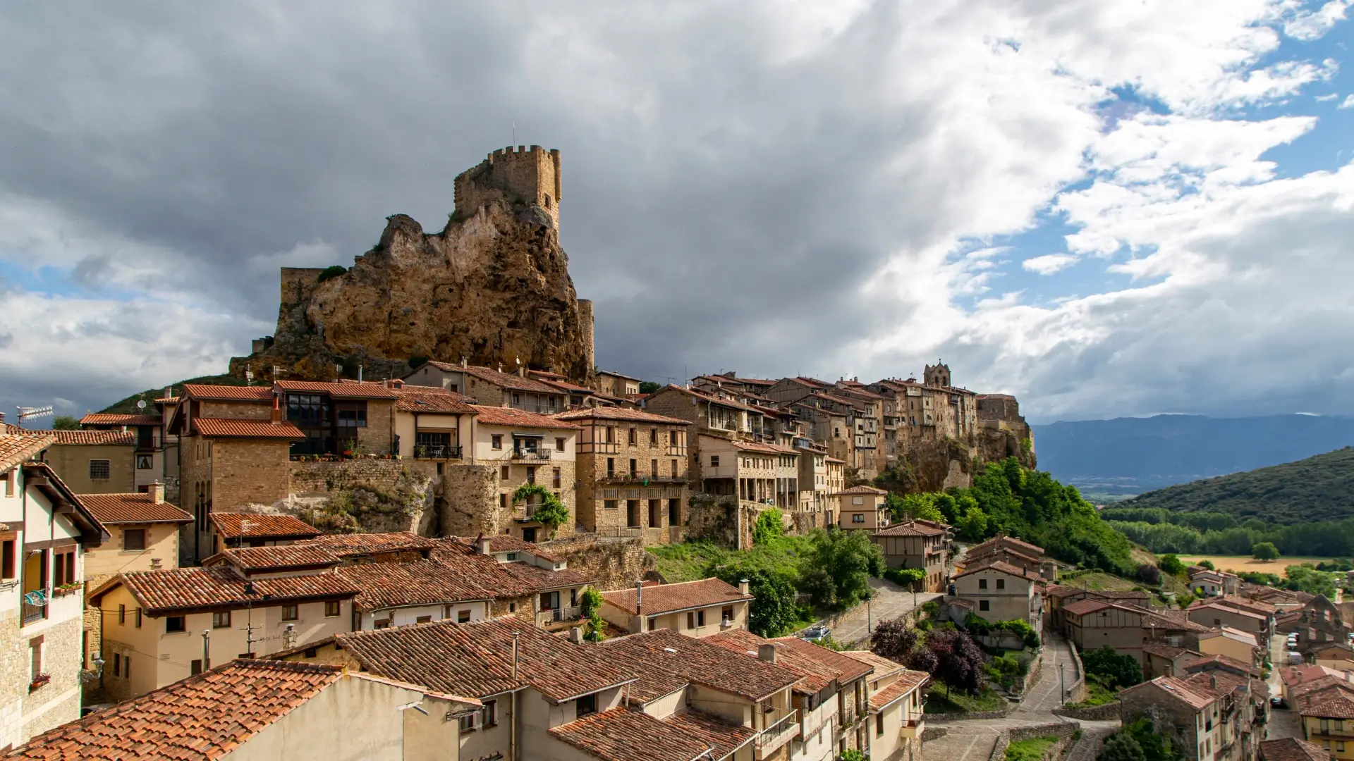 Pueblo medieval con torre de piedra y casas de teja bajo cielo nublado