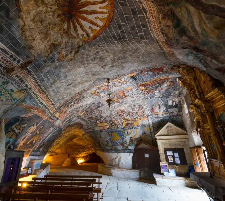 Interior de una capilla con murales medievales y arco dorado al fondo