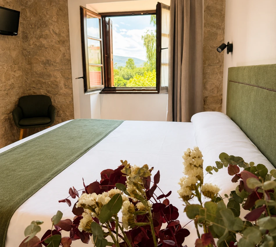 Habitaci&oacute;n con cama doble, flores decorativas y ventana abierta.
