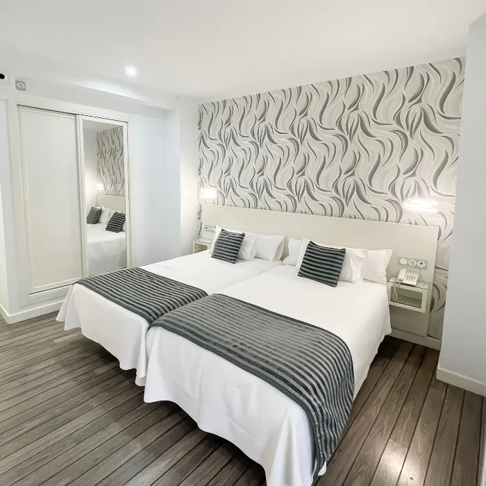 Habitaci&oacute;n moderna con dos camas individuales, decoraci&oacute;n en blanco y gris, y suelo de madera.