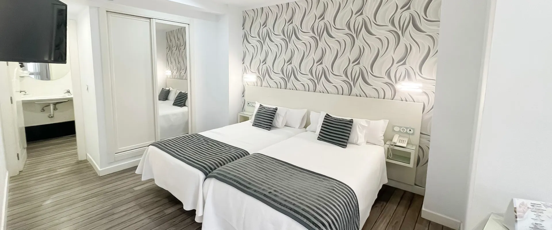 Habitaci&oacute;n con dos camas individuales, decoraci&oacute;n elegante y espejo grande.