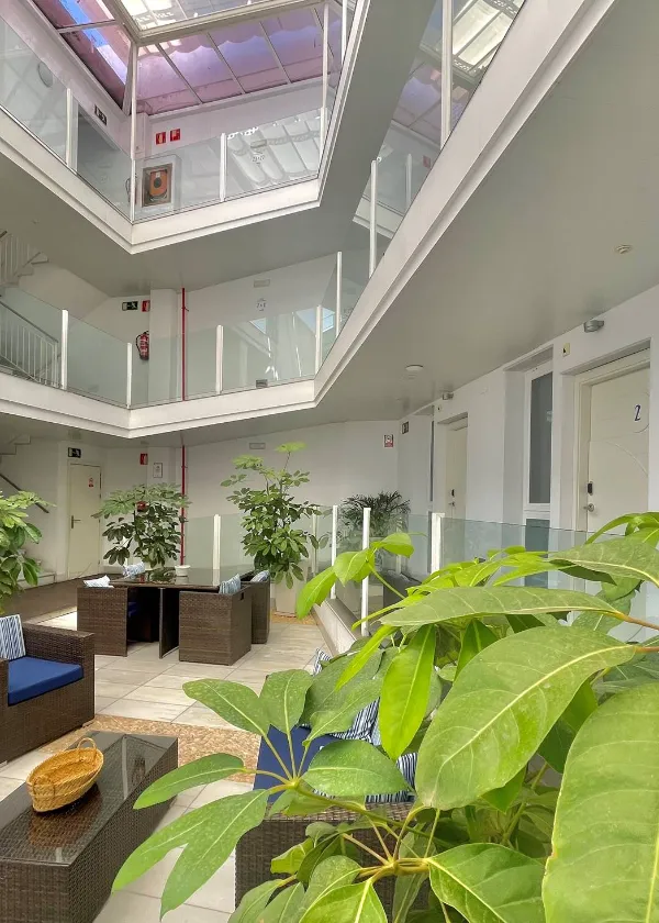 Pasillo interior de un edificio moderno con plantas y muebles de mimbre en la zona de descanso.