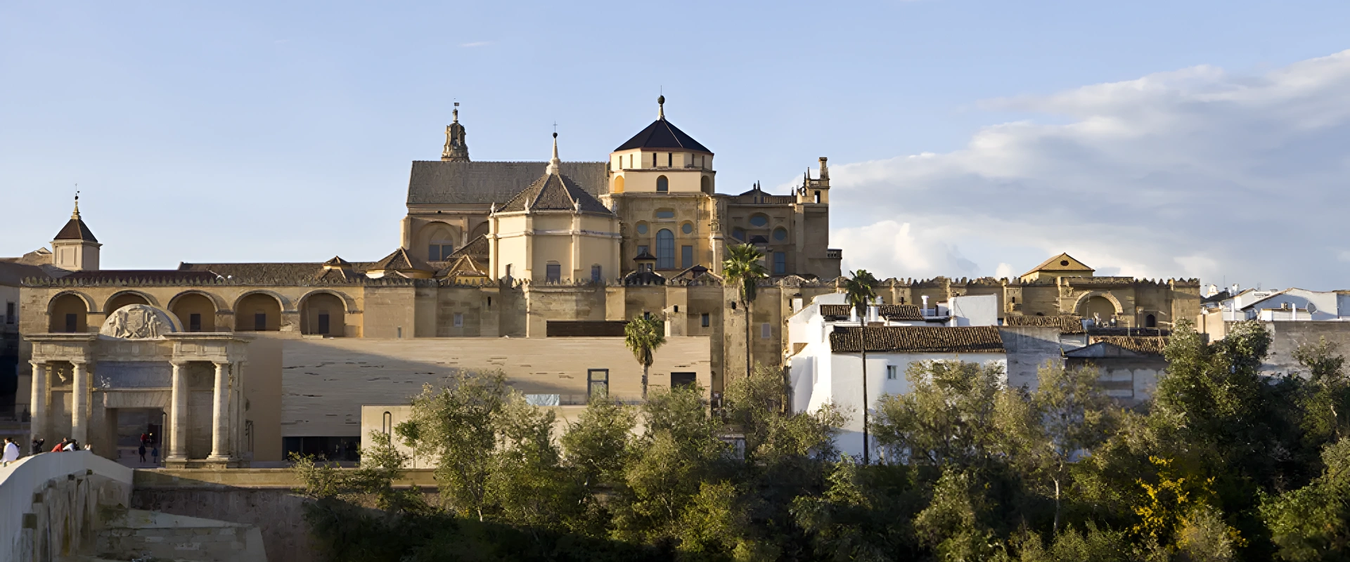 La Mezquita-Catedral de C&oacute;rdoba bajo un cielo azul, con &aacute;rboles en primer plano.