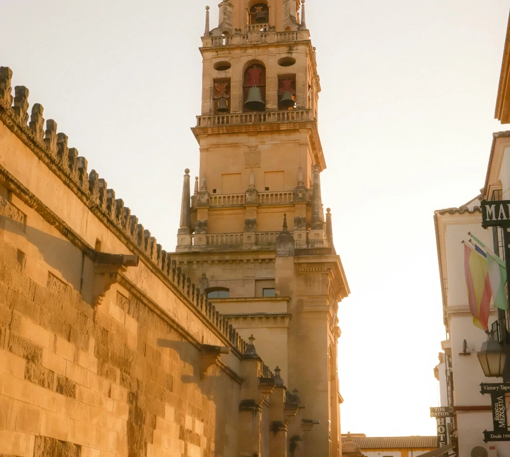 Torre de una iglesia antigua al atardecer, con paredes de piedra y banderas al costado.